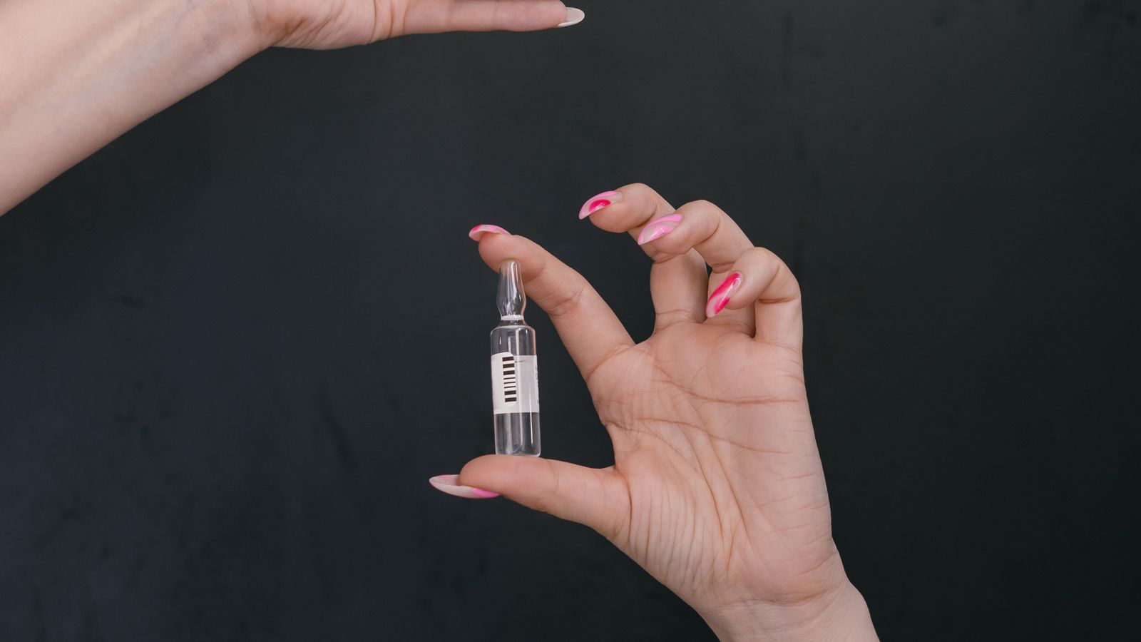 Close-up of hands holding a glucometer, syringe, and ampoule against a dark background.