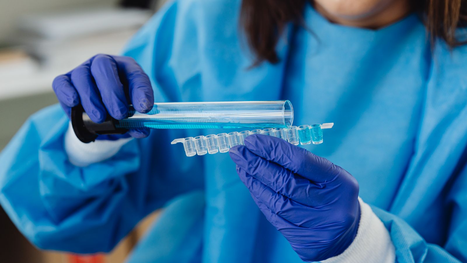 A scientist in blue protective gear examines a row of test tubes and vials during a laboratory analysis.